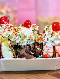 Colorful banana split ice cream sundae topped with whipped cream, cherries, and sprinkles.